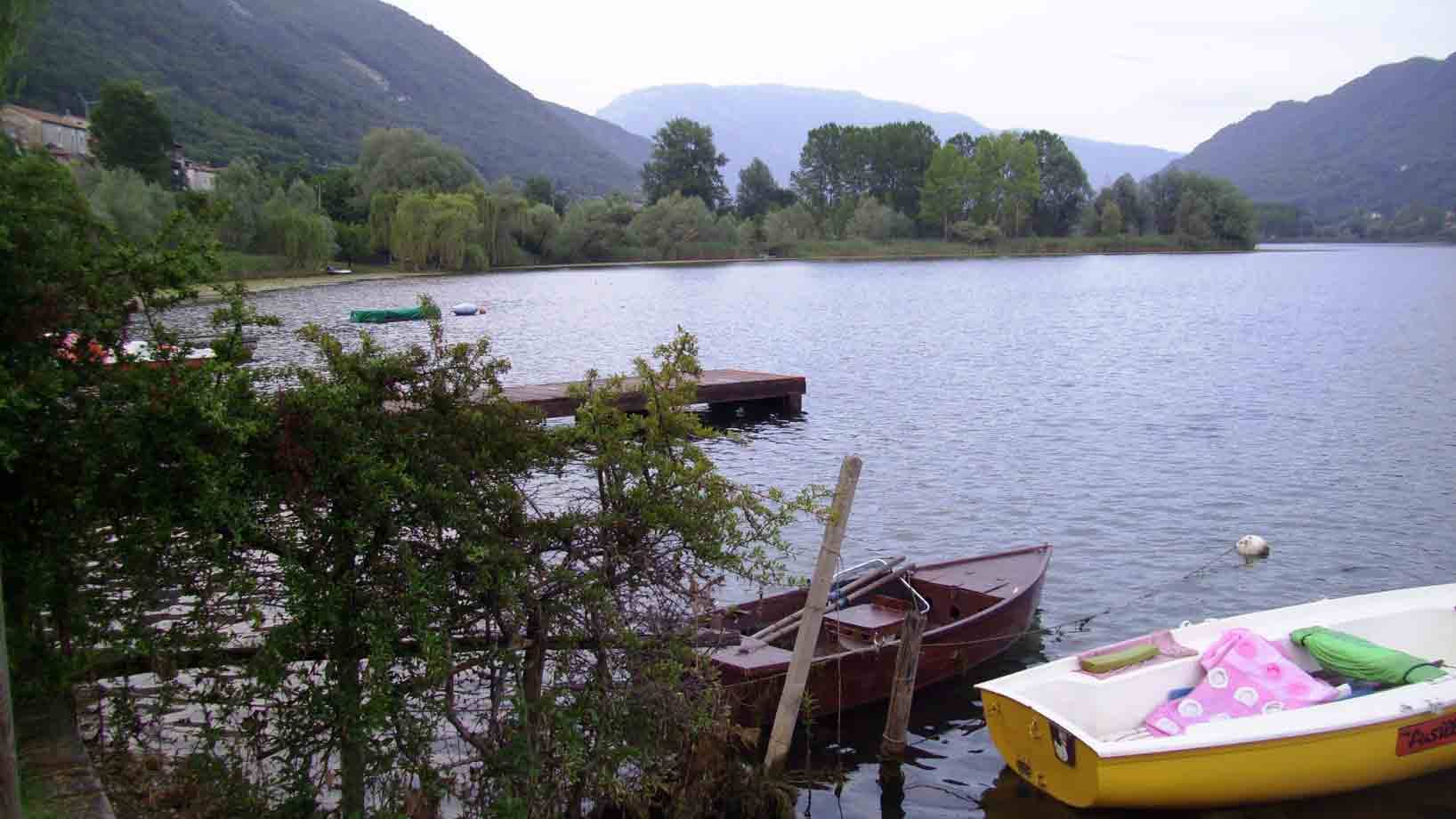 Barche di legno gialle e marroni ormeggiate su lago circondato da montagne verdi
