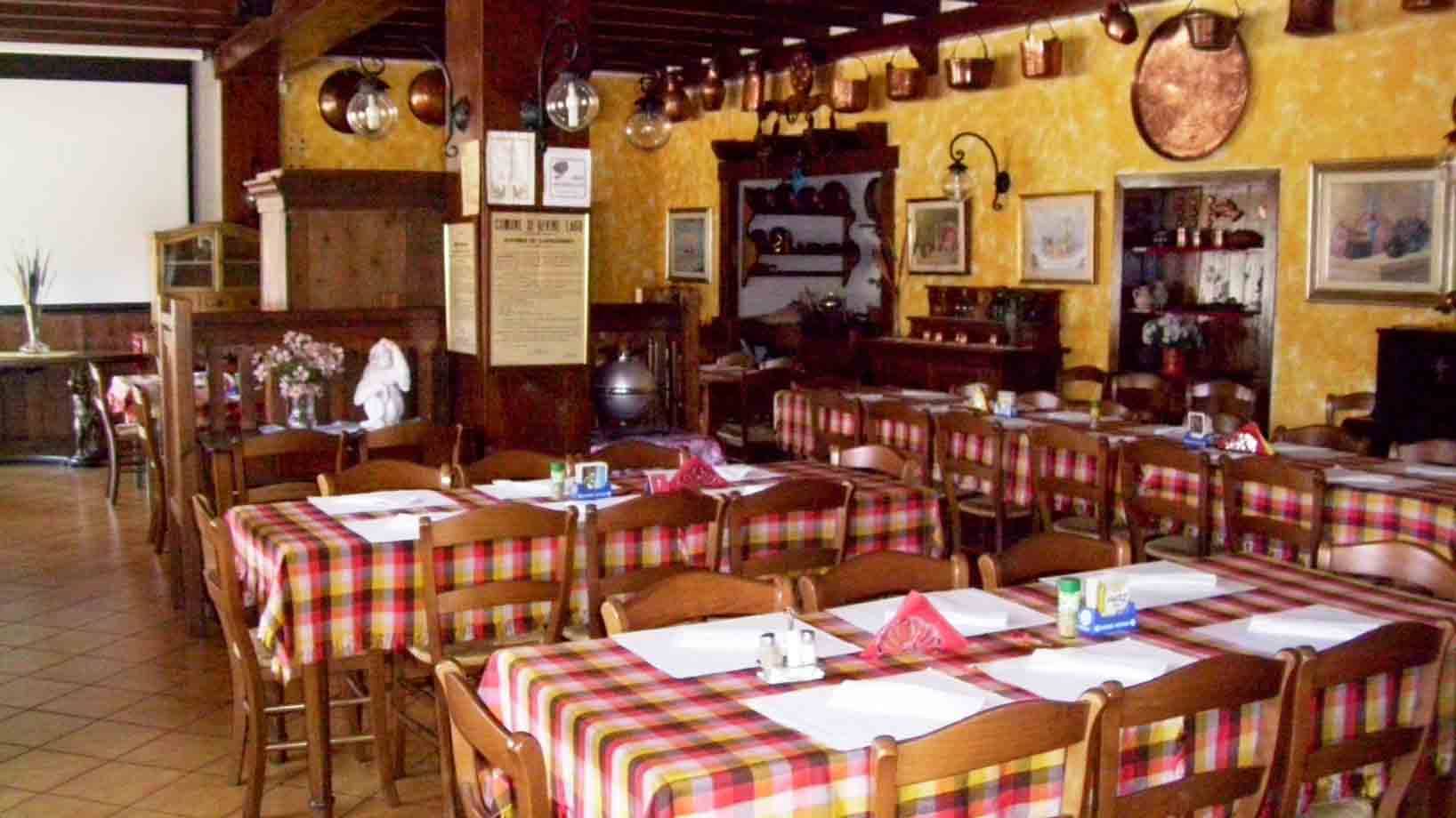 Sala di trattoria con tavoli apparecchiati a tovaglie scozzesi e pentole di rame appese