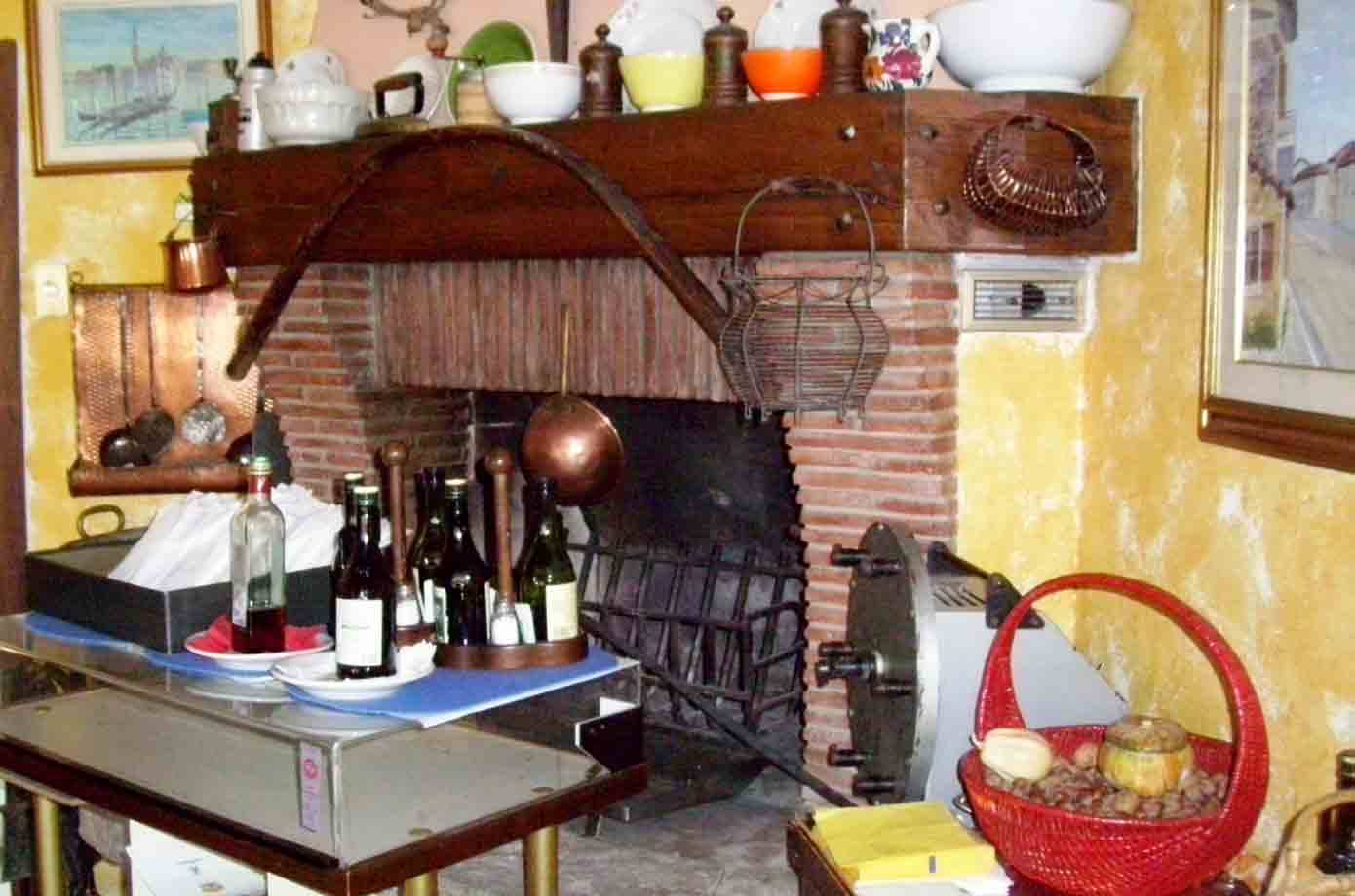 Camino in mattoni con pentole di rame e bottiglie di vino in trattoria