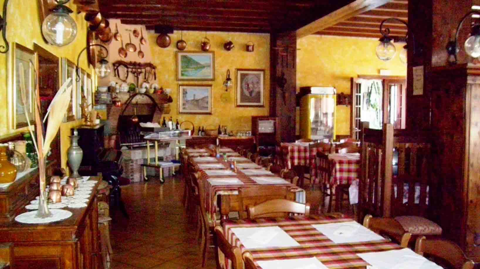 Sala di trattoria con tavoli apparecchiati, tovaglie a quadri, pareti gialle e pentole di rame