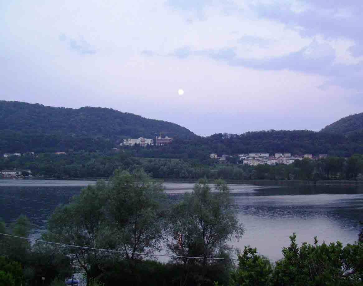 La luna sul lago Circeo circondato da colline alberate
