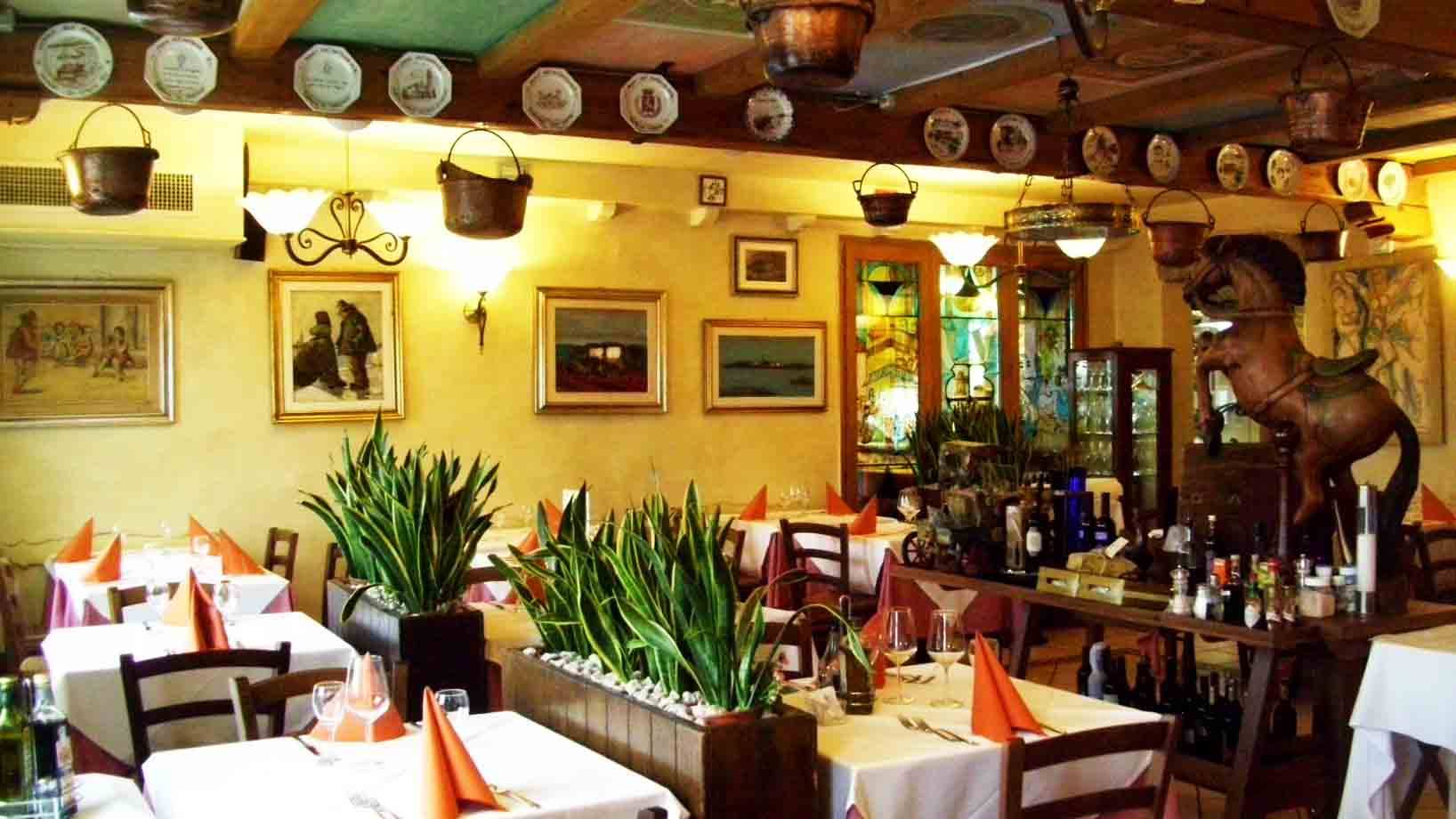 Sala di trattoria con tavoli apparecchiati, piatti decorativi e pentole di rame appese