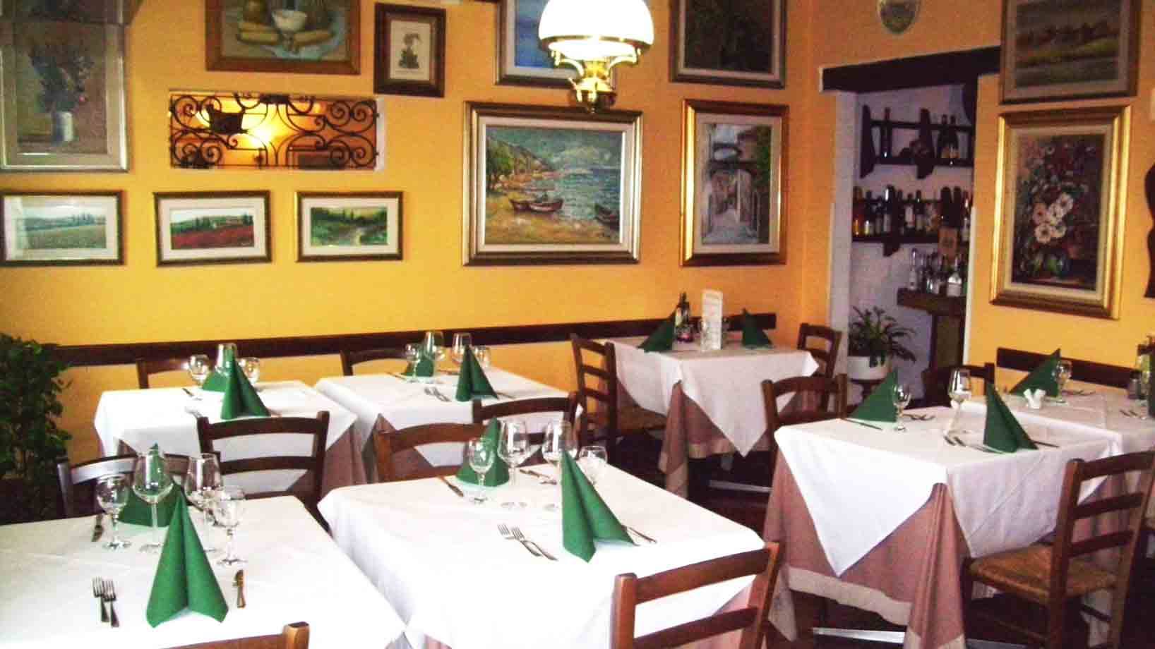 Sala di trattoria con tavoli apparecchiati, tovaglie bianche e quadri sulle pareti gialle