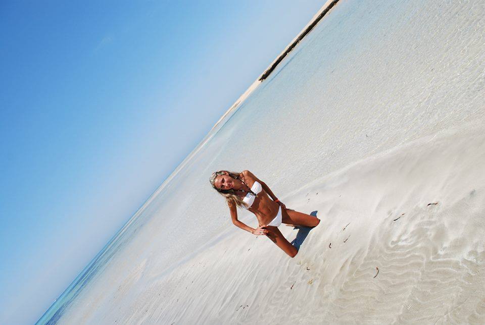 Donna in bikini bianco in ginocchio su sabbia chiara, cielo azzurro