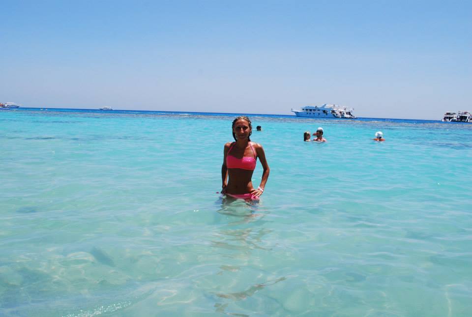 Donna in bikini rosa in acqua turchese con barche da diporto sullo sfondo