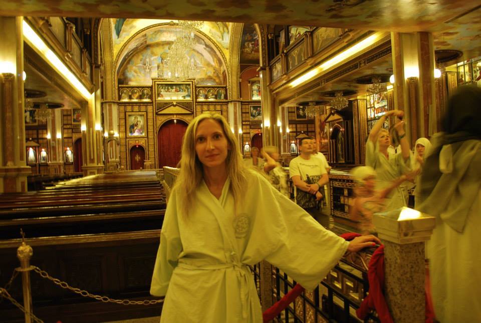 Donna in veste chiara dentro una chiesa ortodossa con mosaici dorati e icone