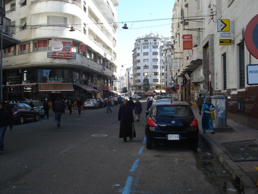 Pedoni e auto parcheggiate in via cittadina con palazzi anni '50, Casablanca