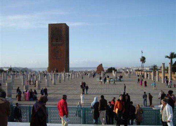 Visitatori sulla vasta platea in pietra della Torre Hassan, colonne incomplete e cielo azzurro a Rabat