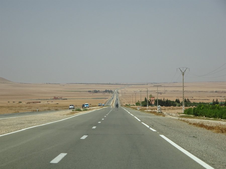 Strada dritta nel sud marocchino verso Errachidia, auto e tralicci tra campi aridi