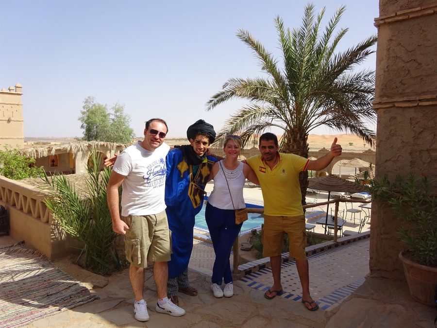 Turisti con guida in abito tradizionale tra palme e terrazze in terra a Merzouga