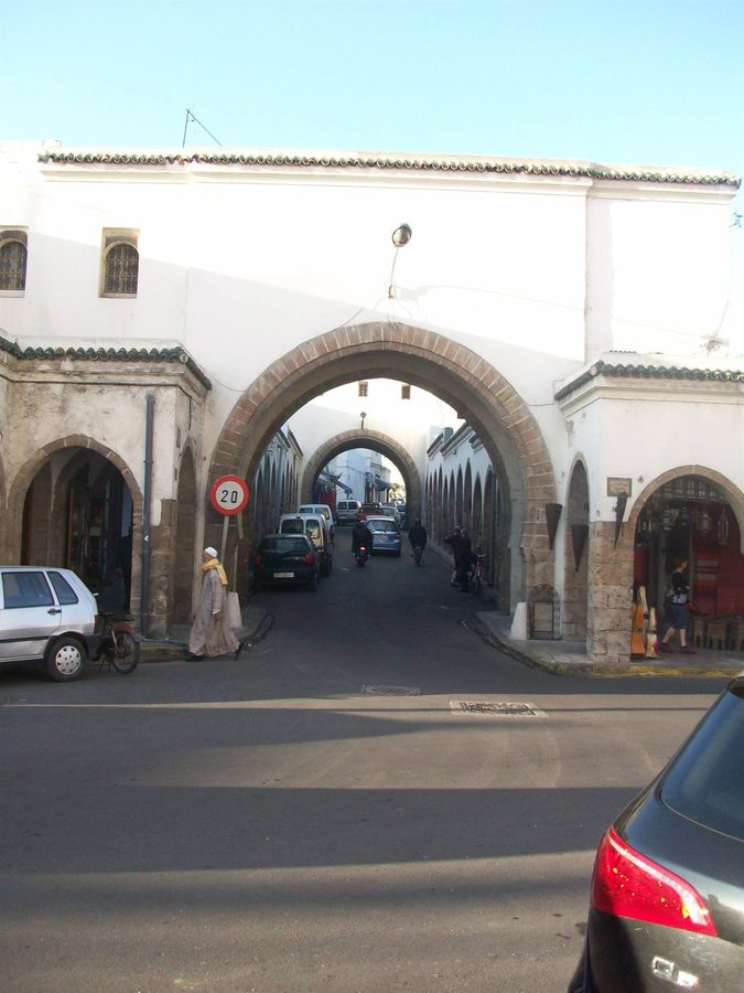 Porta ad arco in pietra su strada con auto e passanti nella medina di Essaouira