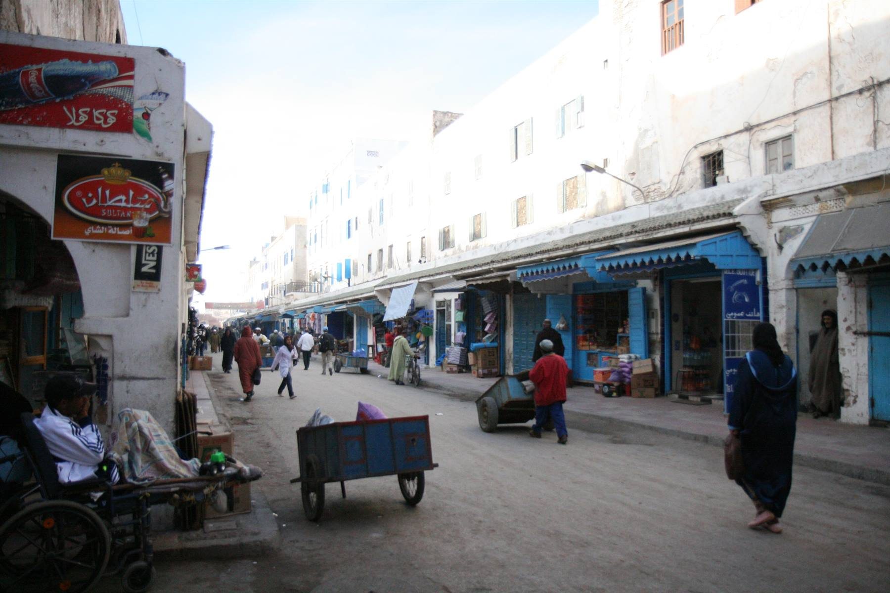 Strada della medina con mercato, carretto blu e passanti tra le mura bianche, Essaouira